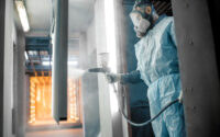 A painter in protective wear sprays on a coating.