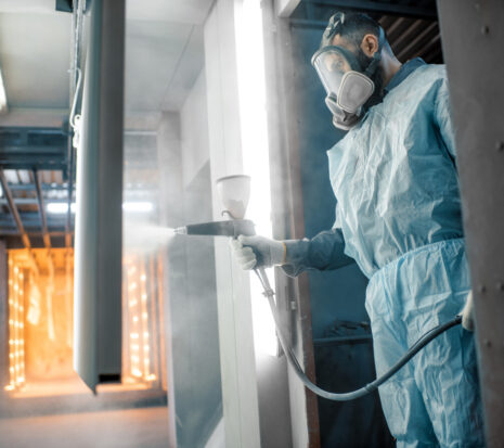 A painter in protective wear sprays on a coating.
